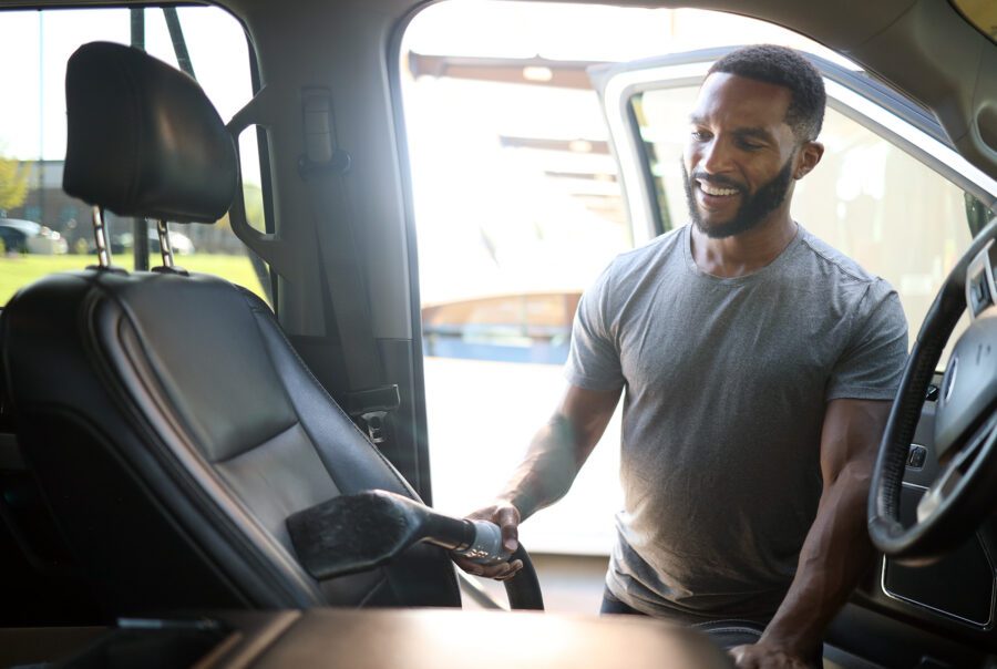 An African American man smiles while he uses the free vacuums at Big Dan's Car Wash to clean his car's black leather interior.